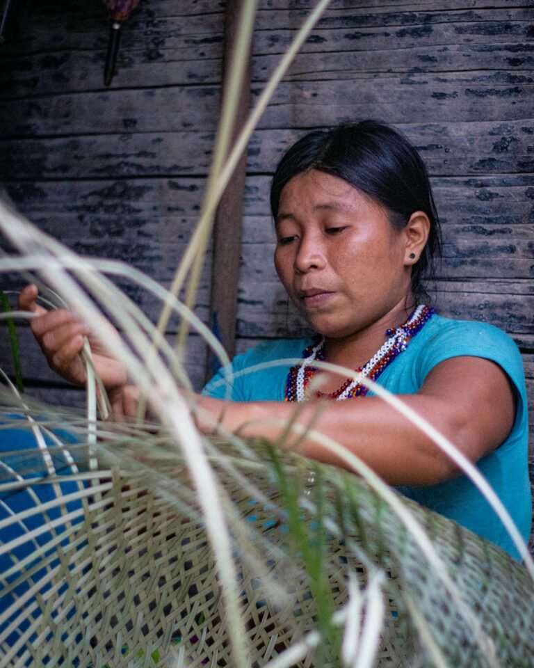 A young woman from Colombia skillfully weaves traditional crafts in an indoor setting.