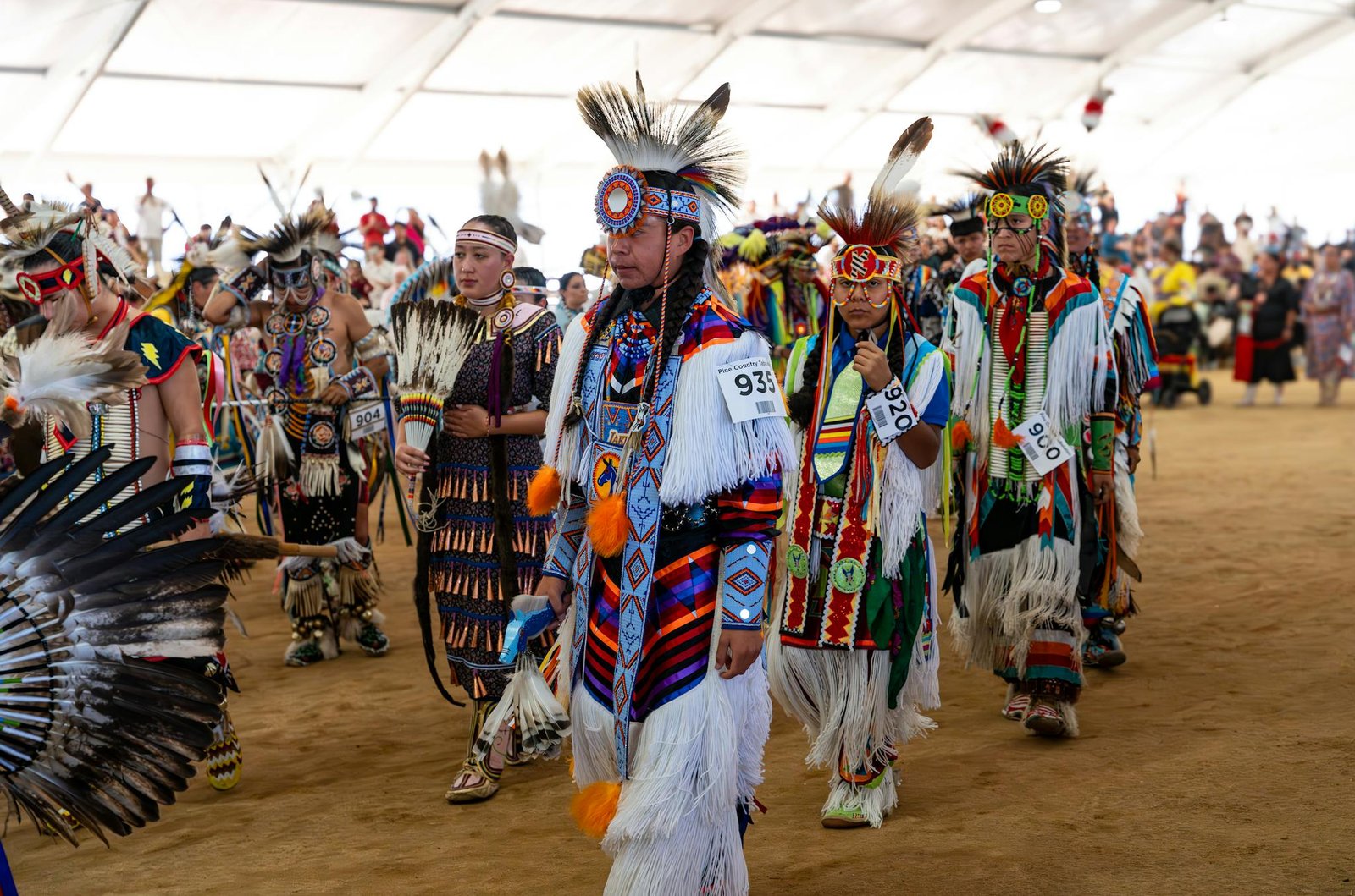Native American dancers in colorful traditional attire at a vibrant pow wow gathering.