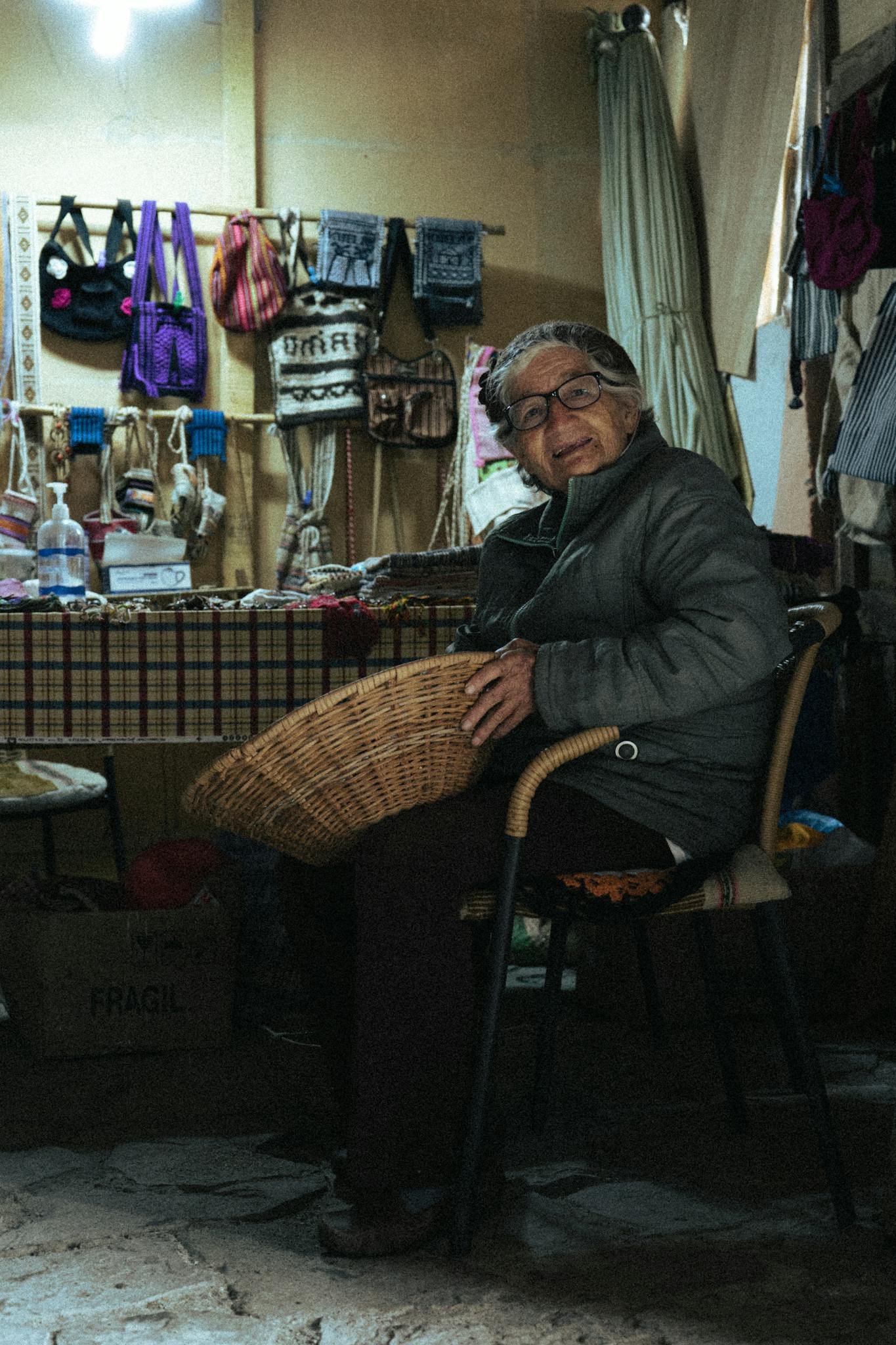 Senior woman weaving a basket in a traditional Peruvian market setting.