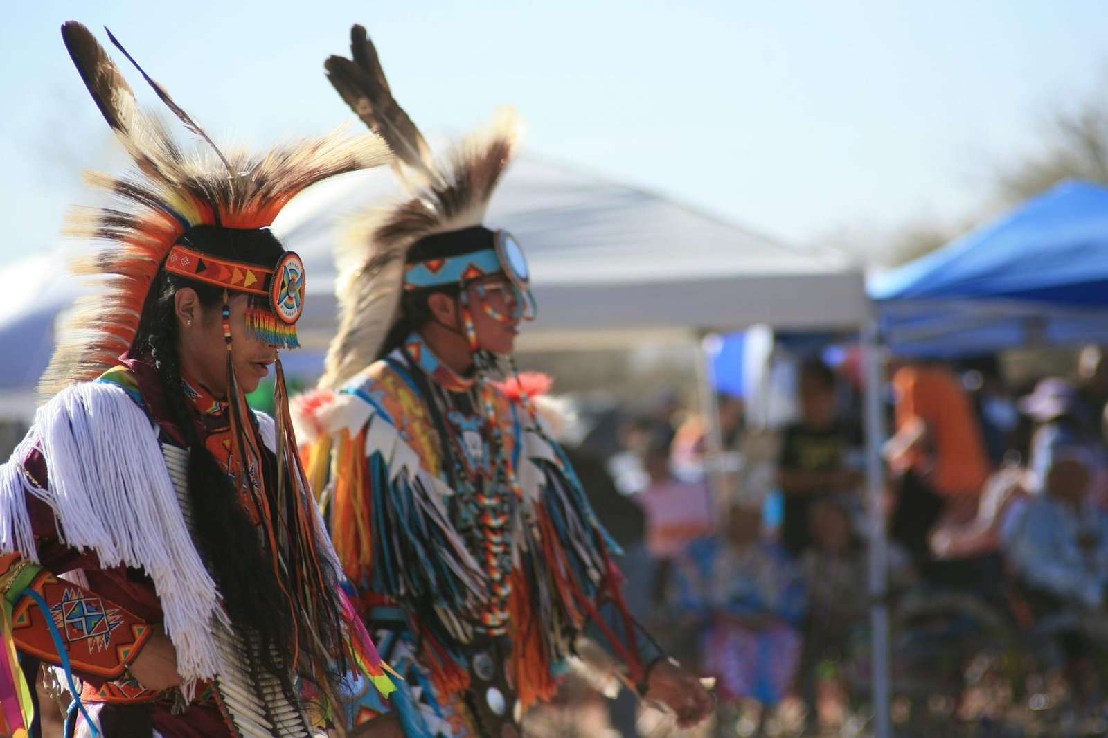 Two Native American dancers in vibrant regalia performing a traditional dance outdoors.